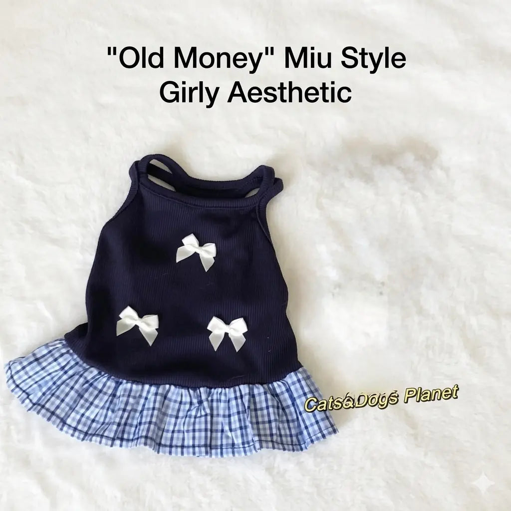 Flat lay of a luxury pet outfit set featuring a navy blue ribbed knit dress with white bows and a gingham ruffle hem, accompanied by a pearl necklace with a bow pendant and tortoise shell pet glasses on a soft cream textured background.